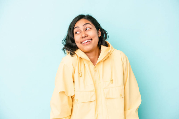 Junge lateinamerikanische Frau auf blauem Hintergrund lacht und schließt die Augen, fühlt sich entspannt und glücklich. - Foto, Bild