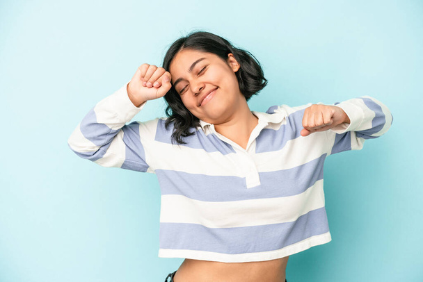Young latin woman isolated on blue background stretching arms, relaxed position. - Photo, Image