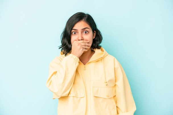 Junge lateinische Frau isoliert auf blauem Hintergrund bedeckt Mund mit Händen, die besorgt aussehen. - Foto, Bild