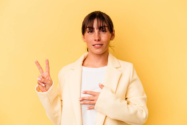 Young Argentinian woman isolated on yellow background taking an oath, putting hand on chest. - Photo, Image