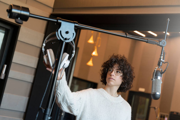 Una joven cantante de pelo rizado con gafas grabando una canción en un estudio real  - Foto, Imagen