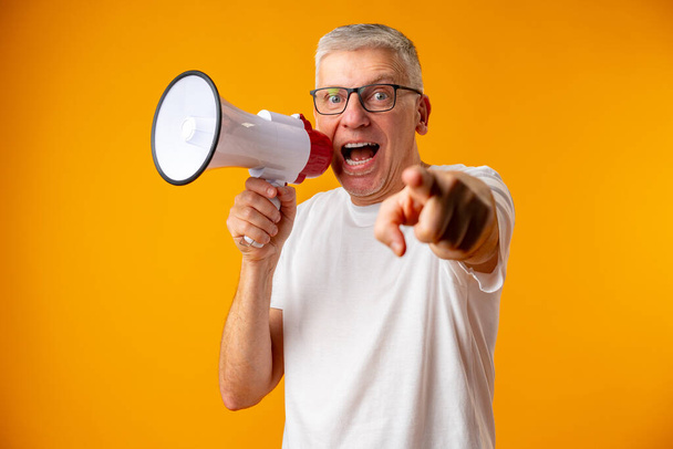 Portrait of mature man shouting with megaphone against yellow background - Фото, изображение