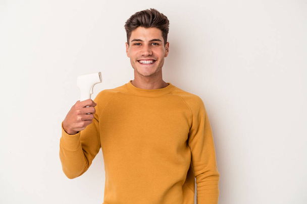 Young caucasian man holding thermometer isolated on white background happy, smiling and cheerful. - Foto, Imagem