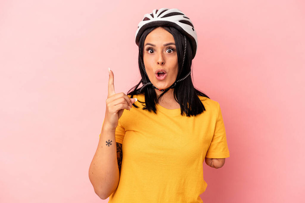 Молода біла жінка з однією рукою в велосипедному шоломі ізольована на рожевому тлі, має ідею, концепцію натхнення
. - Фото, зображення