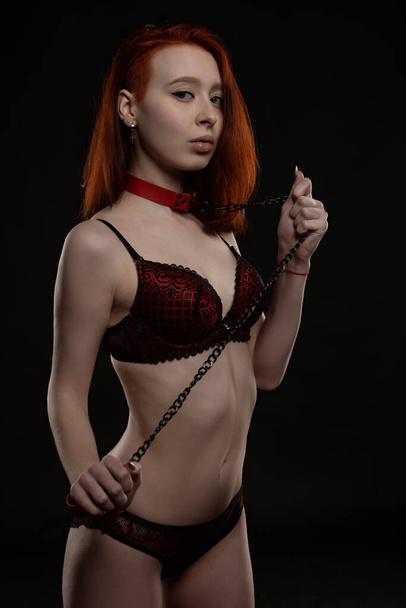A beautiful sexy girl in underwear and with a chain collar around her neck. Studio photo on a dark background - Foto, Imagen