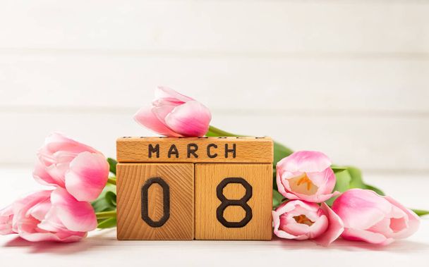 Journée internationale de la femme.Belle carte pour le 8 mars.Bouquet de printemps de tulipes roses avec un calendrier en bois sur un bois texturé blanc. Concept de vacances.Espace de copie. - Photo, image