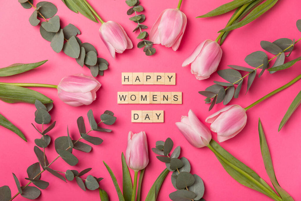 Día Internacional de la Mujer. Bonita postal para el 8 de marzo. Ramo de primavera de tulipanes rosados y eucaliptos con la inscripción feliz día de la mujer sobre un fondo rosado. Concepto de vacaciones. Copiar el espacio.Flatley - Foto, imagen