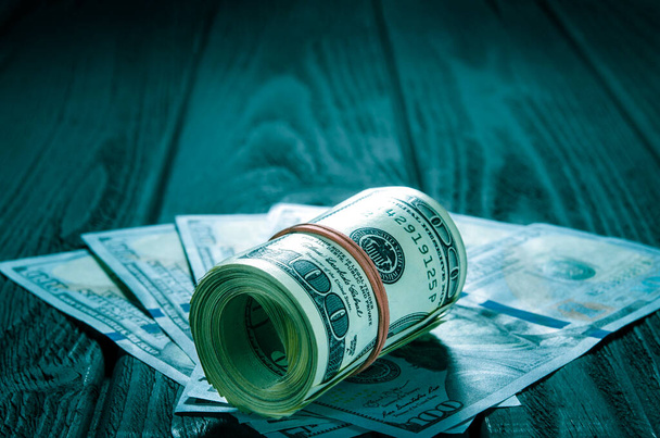 A roll of dollar bills and coins over other bills on a desk. Highlight for the hundred dollar bill. A thick roll of old hundred dollar banknotes tied a red rubber band lies on the whisker of new hundred dollar bills - Photo, Image