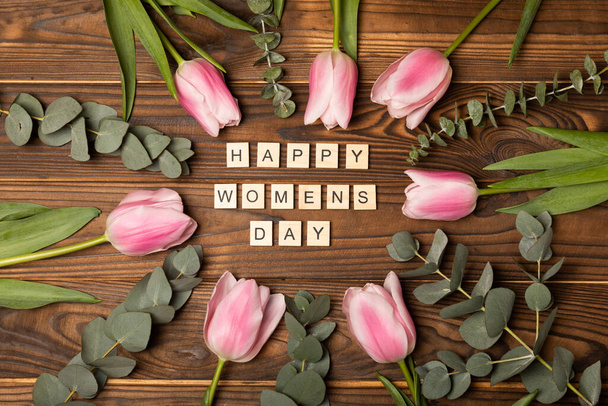Día Internacional de la Mujer Hermosa tarjeta para el 8 de marzo.Ramo de tulipanes rosados con el texto feliz día de la mujer en una madera de textura marrón. Concepto de vacaciones. Copiar el espacio. Vista superior. - Foto, imagen