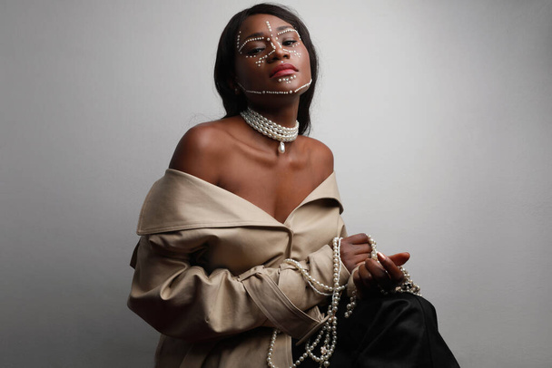 Beautiful African black woman with pearls on her skin posing over grey wall. - Фото, зображення