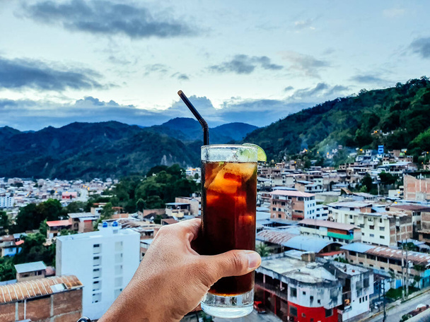 Hand van een man met een drankje met uitzicht op de stad Chanchamayo gelegen in het departement Junin in Peru. - Foto, afbeelding