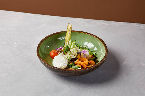 Salad bowl with salmon, avocado, broccoli, vegetables and egg on homemade ceramic plate. Buddha bowl with salmon, broccoli, quinoa in modern serveware. Modern ceramic dishware on concrete background - Фото, изображение