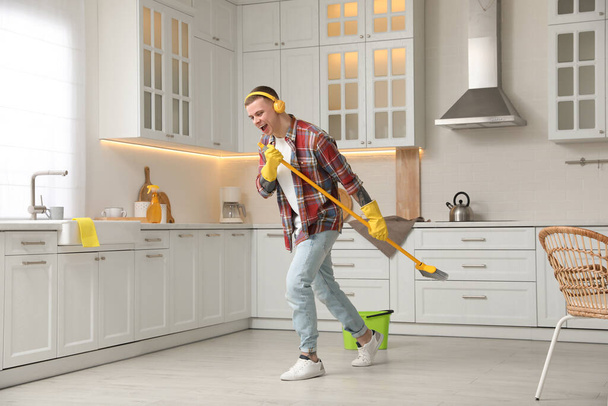 Handsome young man with headphones singing while cleaning kitchen - Foto, Bild