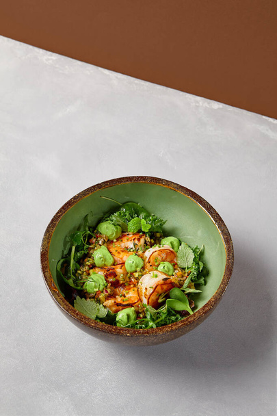 Green bowl with prawns, quinoa and avocado cream on handmade ceramic plate. Salad with shrimp in dark modern dishware. Healthy food in contemporary style. - Фото, изображение