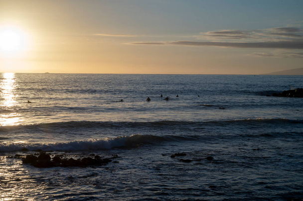 Група серферів подорожує холодною водою Атлантичного океану під час заходу сонця в зимовий час, Playa de las Americas, на південь від Тенерифе. - Фото, зображення