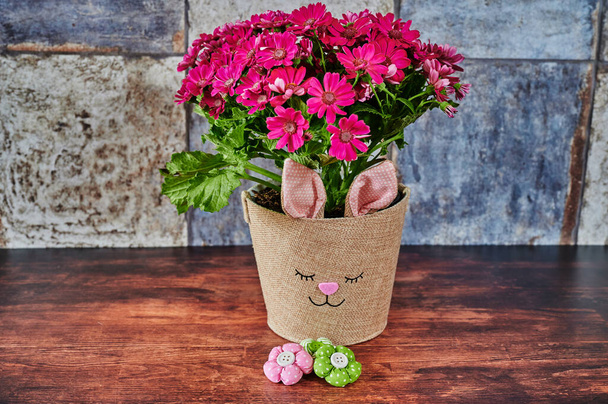 Maceta con una cara de conejo y pequeñas flores de tela en foco. - Foto, imagen
