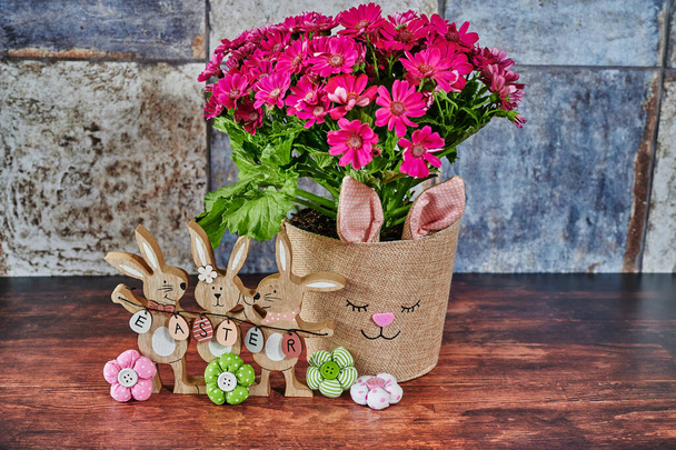 Flowerpot with a rabbit's face and wooden Easter bunnies with the text Easter on the Easter eggs in focus. - Photo, Image