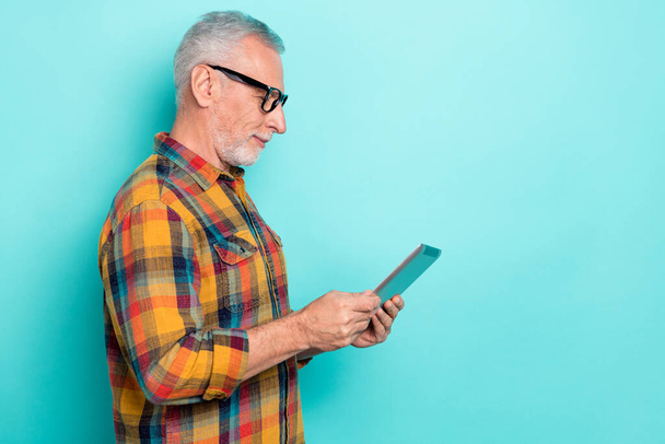 Photo of cheerful man pensioner dressed checkered shirt glasses reading device empty space isolated teal color background - Photo, Image