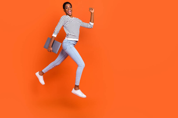 Photo of funny hurrying butch lady dressed sweater jumping holding gadget empty space isolated orange color background - Zdjęcie, obraz