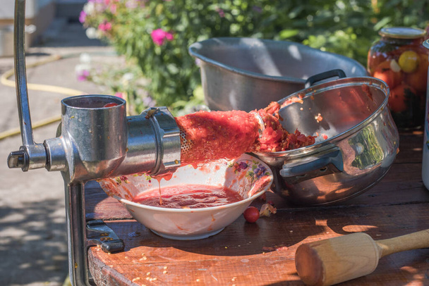 Hausgemachter Tomatensaft wird in einer Handpresse mit einer Schraube gepresst Kinder helfen, den Stielsaft aus dem Fruchtfleisch durch ein Sieb zu drehen, das Fruchtfleisch wird auf den Kompost geworfen - Foto, Bild