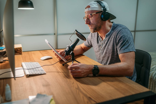 Middle-aged Blogger man in headphones reading text recording voice or making online webinar or news announcement. Modern home sound studio audio recording or live streaming technology concept. - Zdjęcie, obraz