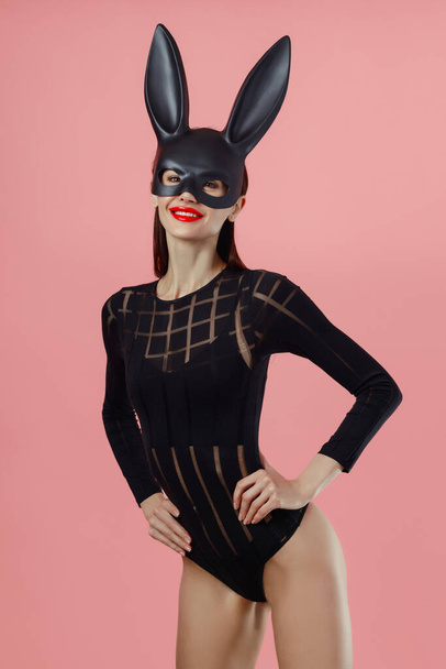 Sexy woman wearing a black mask Easter bunny standing on a pink background and looks very sensually. - Foto, immagini