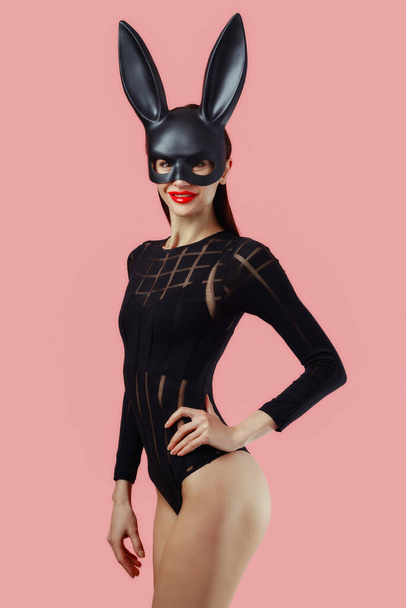 Sexy woman wearing a black mask Easter bunny standing on a pink background and looks very sensually. - Valokuva, kuva