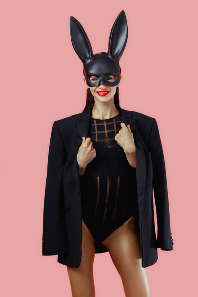 Sexy woman wearing a black mask Easter bunny standing on a pink background and looks very sensually. - Фото, зображення