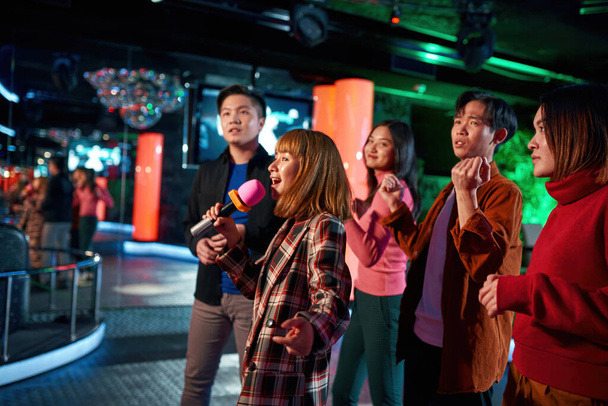 Gruppe junger Leute singt auf der Bühne eines Karaoke-Clubs - Foto, Bild