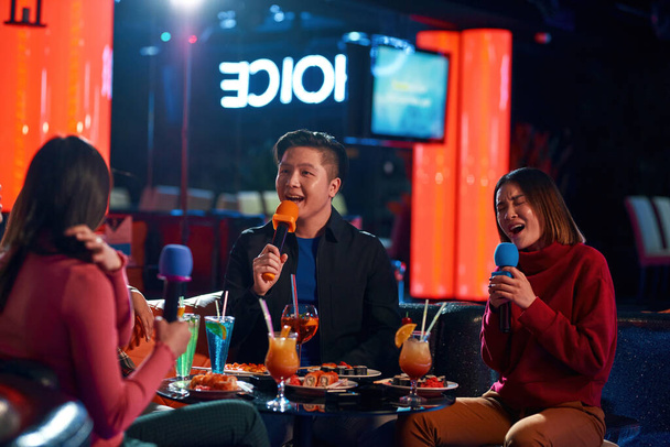 Asian friends having fun while singing karaoke on night party at the bar - Fotó, kép