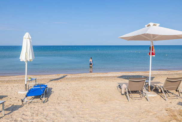 Schöne Ansicht der Frau, die in ruhigem Meerwasser steht und am Horizont auf weißen Sandstrand und Sonnenschirme blickt. Griechenland.  - Foto, Bild