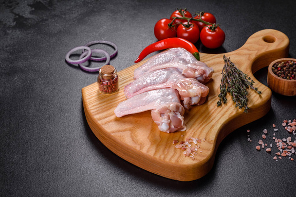 Ωμό κρέας. Φτερούγες κοτόπουλου βρίσκονται σε ξύλινη σανίδα με λαχανικά και μπαχαρικά σε μαύρο φόντο - Φωτογραφία, εικόνα