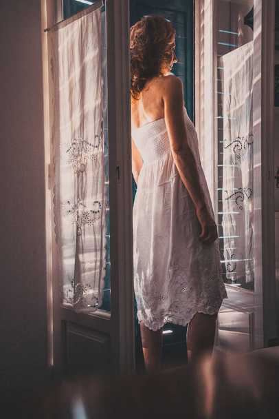γυναίκα σε λευκό φόρεμα καλοκαίρι άνοιγμα μπαλκονόπορτα - Φωτογραφία, εικόνα