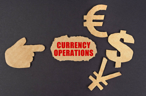 Economy and finance concept. On a black surface, a figure of a hand, money symbols and torn cardboard with the inscription - currency operations - Φωτογραφία, εικόνα