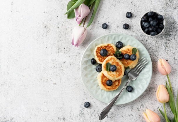 Cottage cheese fritters with blueberries on ceramic blue plate on concrete background. Healthy calcium breakfast, lunch or snack. Traditional russian food. Close up - Фото, изображение