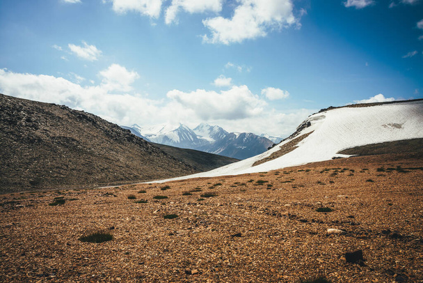 Landschaftlich reizvolle Hochlandlandschaft mit Gletscher auf Hügeln vor dem Hintergrund eines großen schneebedeckten Berges mit Gipfel in niedrigen Wolken. Toller Blick aus der Hochgebirgswüste auf große schneebedeckte Berge in niedrigen Wolken. - Foto, Bild