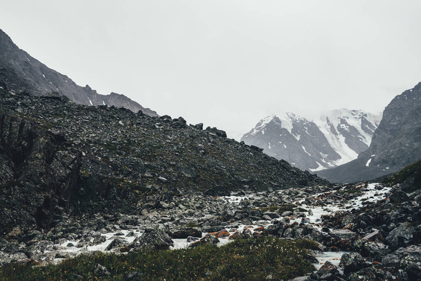 Ατμοσφαιρικό τοπίο με βουνίσιο ρυάκι μεταξύ των Μοραΐνων σε βροχερές καιρικές συνθήκες. Bleak τοπίο με γαλακτώδες ποτάμι από χιονισμένα βουνά. Πέτρες με βρύα και λειχήνες στο ρυάκι του νερού. Ορεινός ποταμός ανάμεσα σε βράχια. - Φωτογραφία, εικόνα