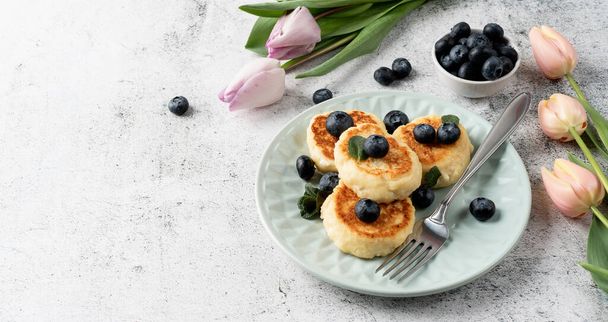 Cottage sajt fritterek áfonyával kerámia kék lemez beton alapon. Egészséges kalcium reggeli, ebéd vagy snack. Hagyományos orosz étel. Közelről. - Fotó, kép