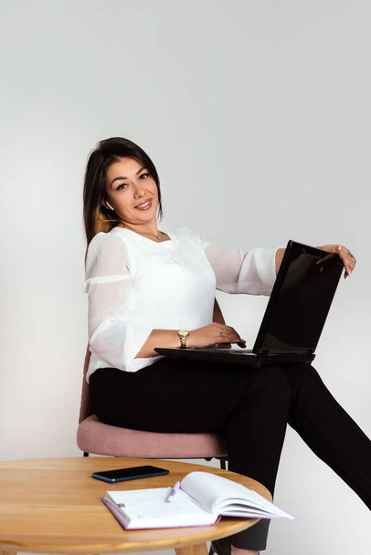 Full length portrait of smiling business woman sitting with laptop and looking at camera on white background - Photo, Image