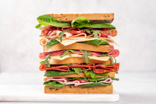 Big tasty sandwich with ham, salami, salad, cheese and tomatoes - Foto, afbeelding