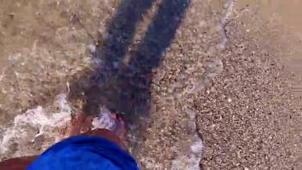 Dziewczyna z gołymi stopami spaceruje po wodzie po piaszczystej plaży morza i chlapie wodą - Materiał filmowy, wideo