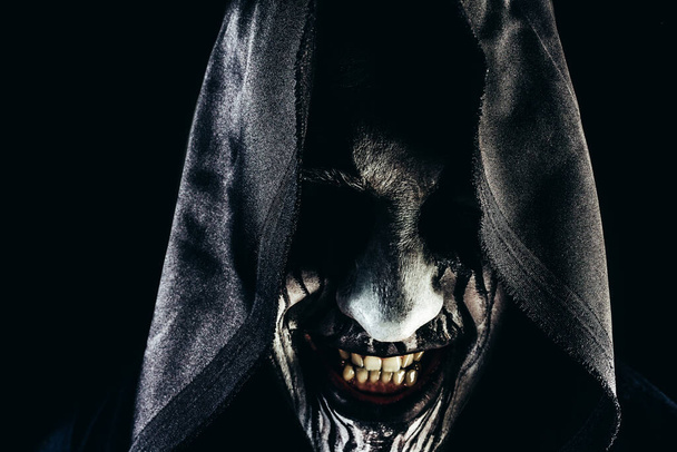 Foto de horror de un hombre monstruo segador sonriendo cara en la capucha sobre fondo oscuro. - Foto, Imagen
