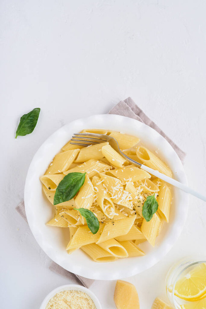 Tasty appetizing classic italian penne pasta with parmesan cheese and basil in white plate on plate on on stone table. Traditional dish of Italian cuisine. Top view. - Photo, image