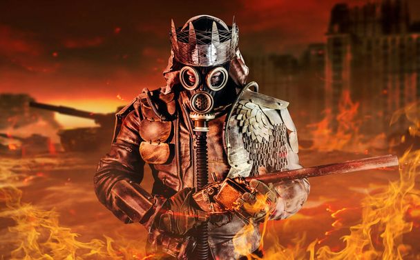 Photo of post apocalyptic warrior with armored outfit jacket and scrap crown standing with rifle on destroyed burning city background. - Photo, Image