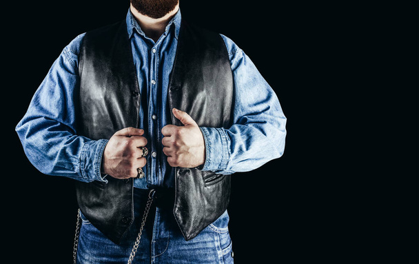 Front view photo of man in jeans shirt, denim pants and leather biker vest standing on black background. - Fotó, kép