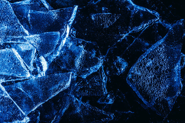 Photo of blue toned frozen cracked ice pieces surface texture on dark backdrop. - Foto, afbeelding