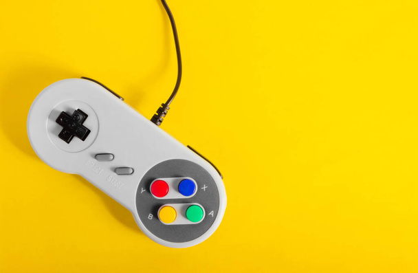 黄色の背景に敷設古典的な灰色の8ビットゲームパッドコントローラの写真. - 写真・画像