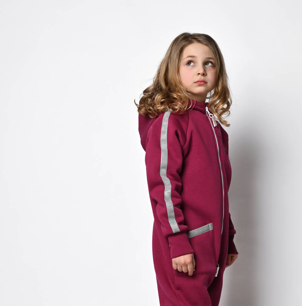 waist-length portrait of a stylish girl in a bordo sports suit with reflective stripes, looks to the side. stylish cotton tracksuit, pajamas with a hood, a fashion model for children - Fotoğraf, Görsel
