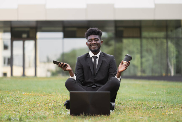 African young business man meditating outside after work in front of company building - Foto, afbeelding