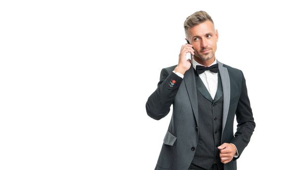 positive businessman in tuxedo speak on phone isolated on white background - Foto, afbeelding
